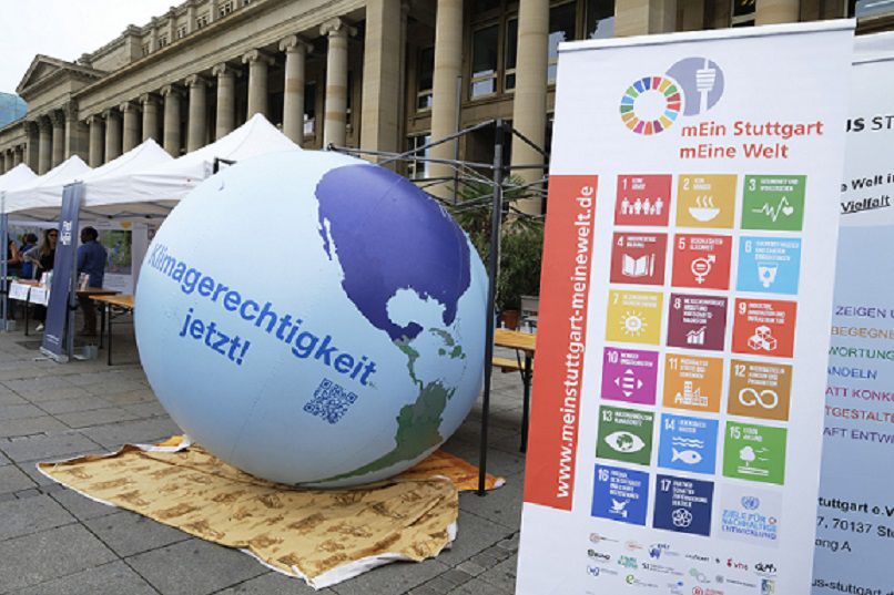 Zu erkennen ist ein Informationsstand mit den 17 SDGs der Nachhaltigkeit auf einem Roll-up und einer Weltkugel nebenan.