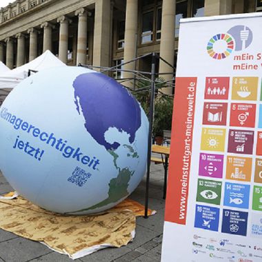 Zu erkennen ist ein Informationsstand mit den 17 SDGs der Nachhaltigkeit auf einem Roll-up und einer Weltkugel nebenan.