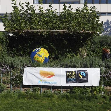 Eine Erdkugel im Garten vor einem grauen Gebäude und einem Plakat der Fairtrade Stadt Ludwigsburg