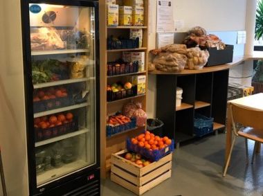 Das Bild zeigt einen Kühlschrank, ein Regal und Kisten mit Gemüse und Obst.