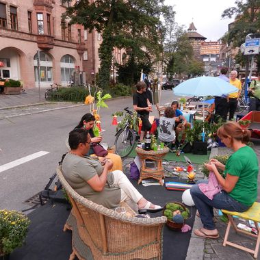 Mehrere Personen sitzen auf Stühlen und Sesseln am Straßenrand und basteln während des Parking Days in Nürnberg